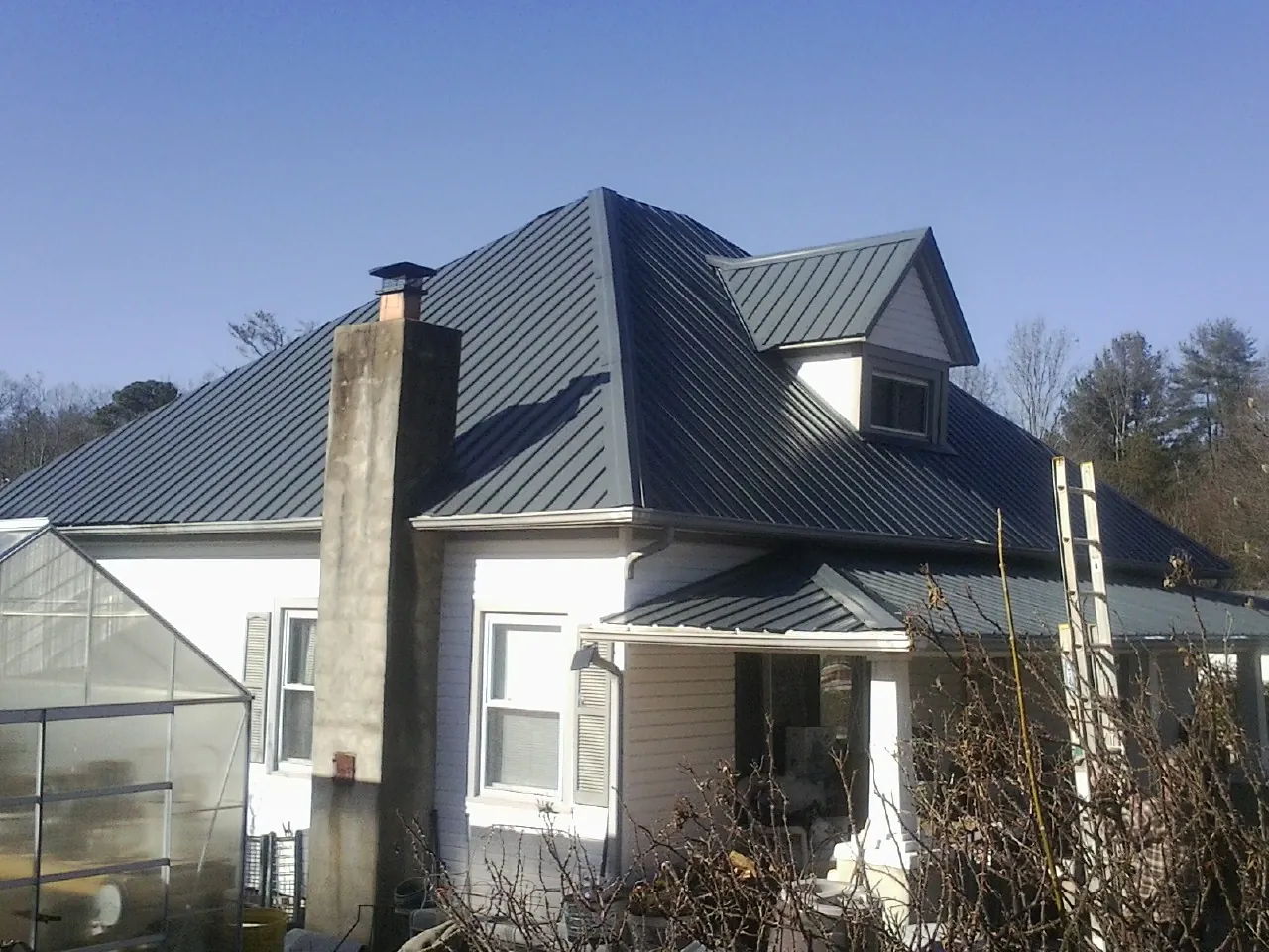 Dark blue standing seam metal roof on a white farmhouse with dormer — Slate & Tile Roof Repair by Roofing Brothers in Landrum