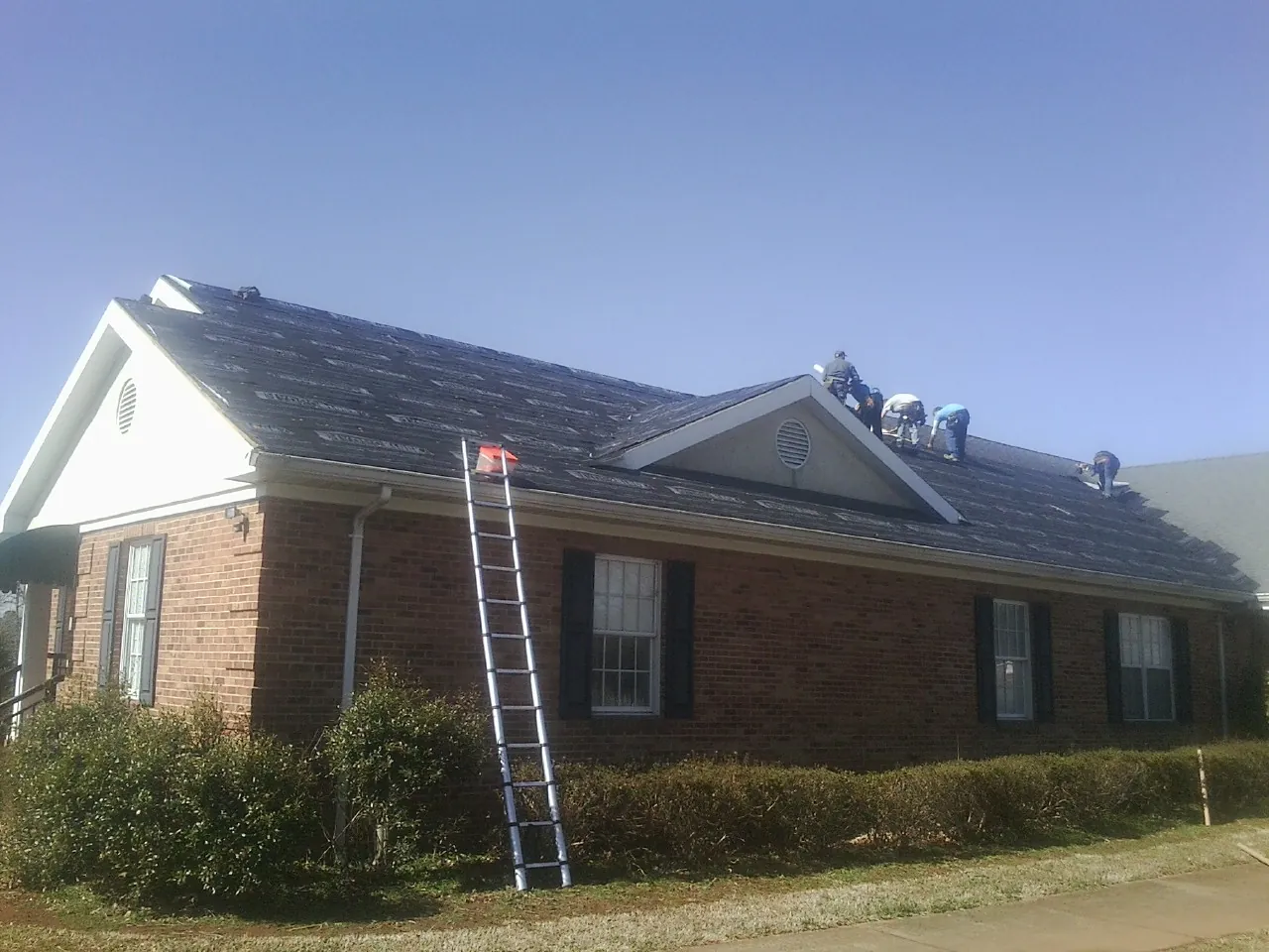 Crew tearing shingles off a brick ranch roof with a ladder set — Emergency Roof Repair work by our crew in Landrum