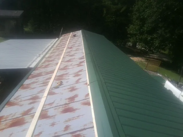 Old rusted panels beside newly installed green metal roofing — Wind Damage Roof Repair by Roofing Brothers in Landrum