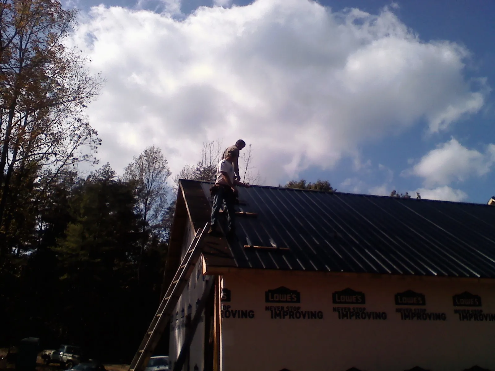 Roofer fastening dark metal panels high against a cloudy sky, from a Roof Inspection job in Landrum