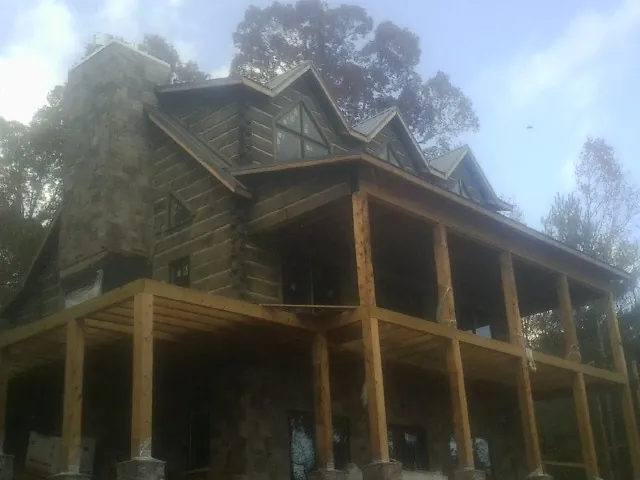 Stone chimney and dormers on a large log home with a timber porch in Landrum