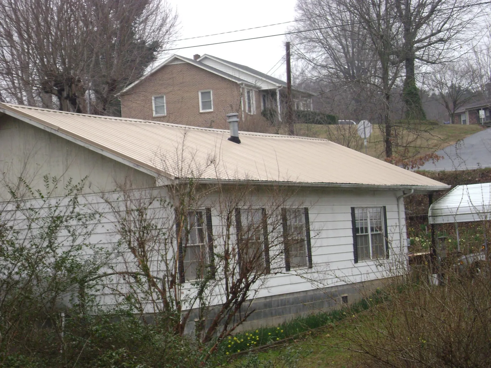 Tan metal roof on a white sided house set into a hillside — Commercial Roofing by Roofing Brothers in Landrum