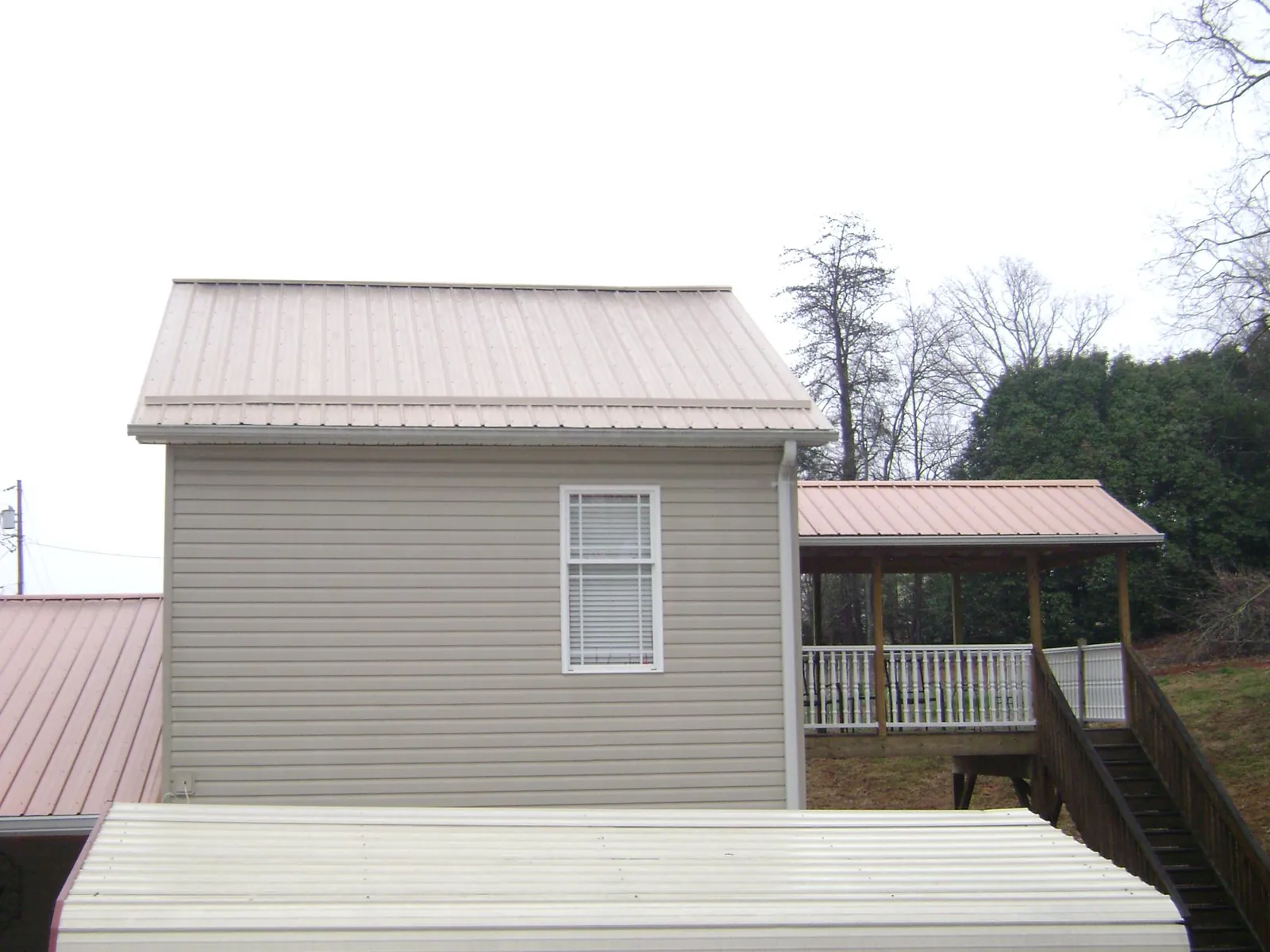 Tan metal roofs on a two story addition and attached porch, from a Roof Replacement job in Landrum